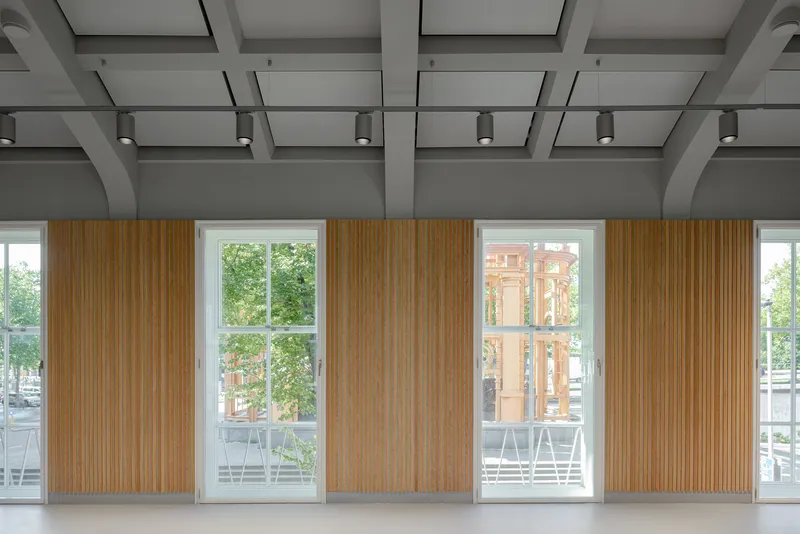 Interior wall with alternating timber slat panels and tall windows framed by coffered grey ceiling