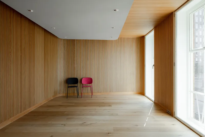 Room with vertical timber slat walls, recessed ceiling panel and two upholstered chairs under natural light