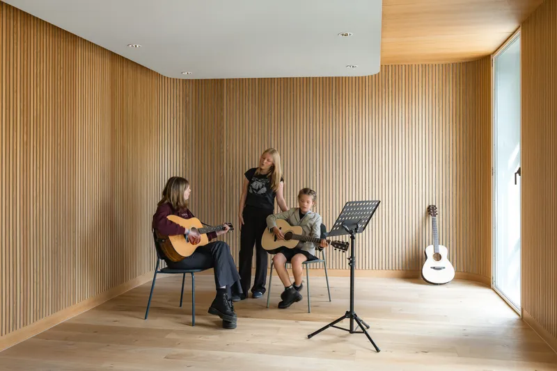 Music lesson in a timber-lined room with three people playing guitars beside a music stand