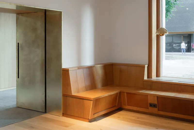 Corner window seat with curved timber paneling and bronze pendant light overlooking the street