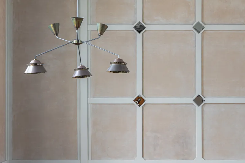 Multi-arm chandelier hanging against wall panel grid with diamond-shaped glass inserts and white trim