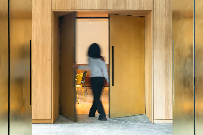 Timber doorway framing a person in motion passing through into a lit interior hallway