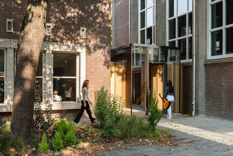 Brick courtyard facade with tall windows and planted beds under dappled tree shadows