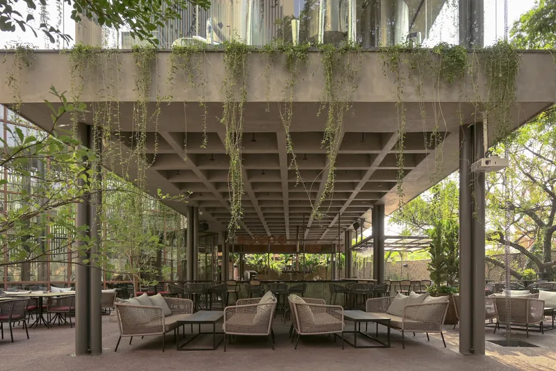 Covered terrace seating beneath a coffered concrete canopy with cascading greenery overhead