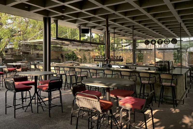 Bar seating area under coffered concrete ceiling with red cushioned stools and filtered afternoon light