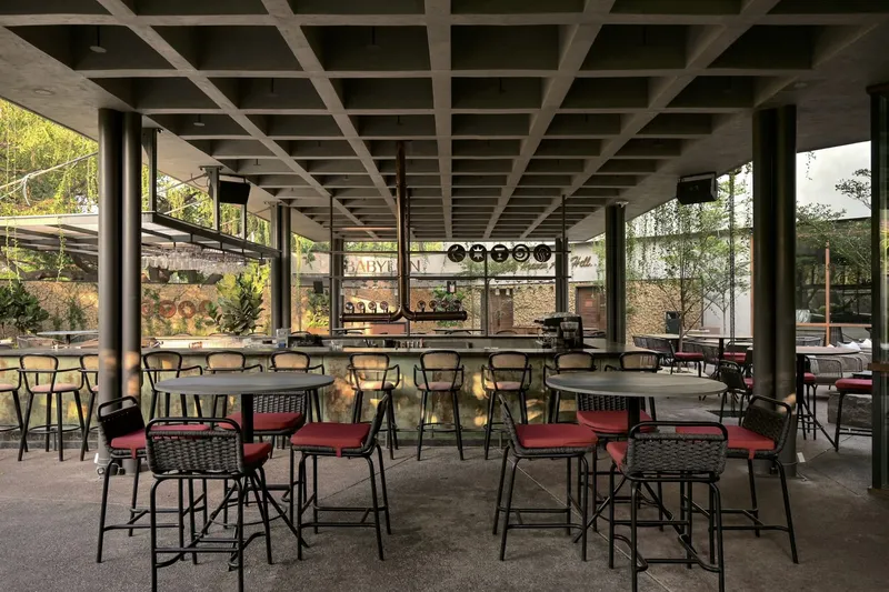 Open-air dining area under concrete waffle slab supported by steel columns with bar visible beyond