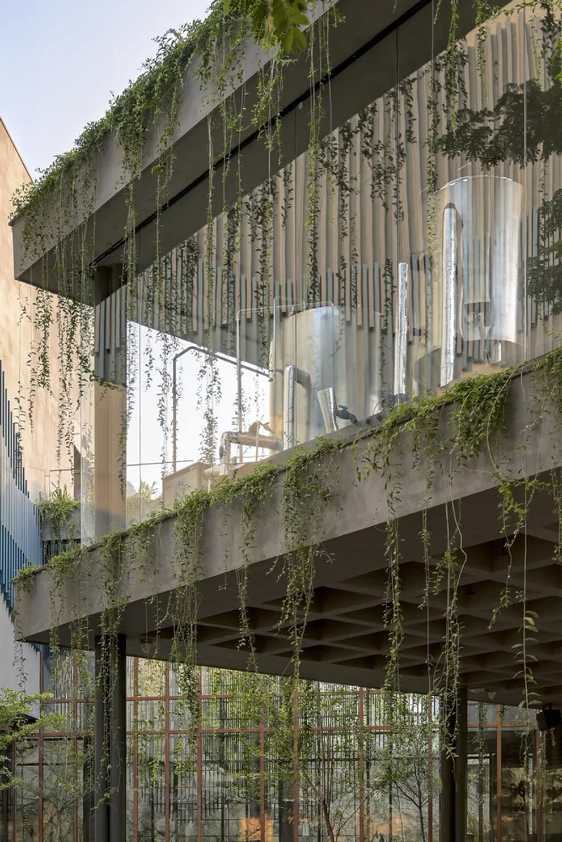 Concrete facade with vertical metal fins and cascading vegetation from the planted terrace above