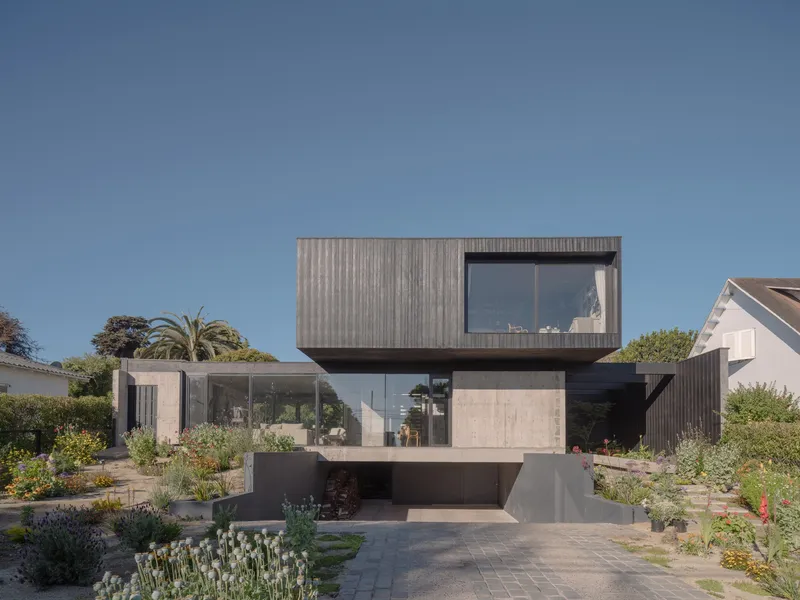 Front facade featuring stacked volumes of vertical timber cladding, concrete, and glass above planted beds with succulents