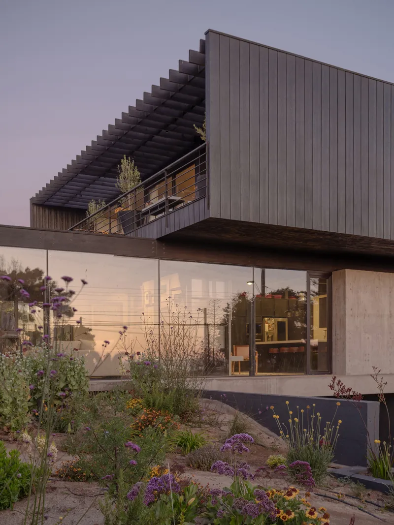 Cantilevered timber-clad volume with slatted pergola above glass-walled living space at dusk