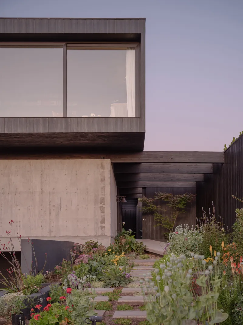 Entrance path of stone pavers through planted garden leading to recessed doorway beneath cantilevered upper volume