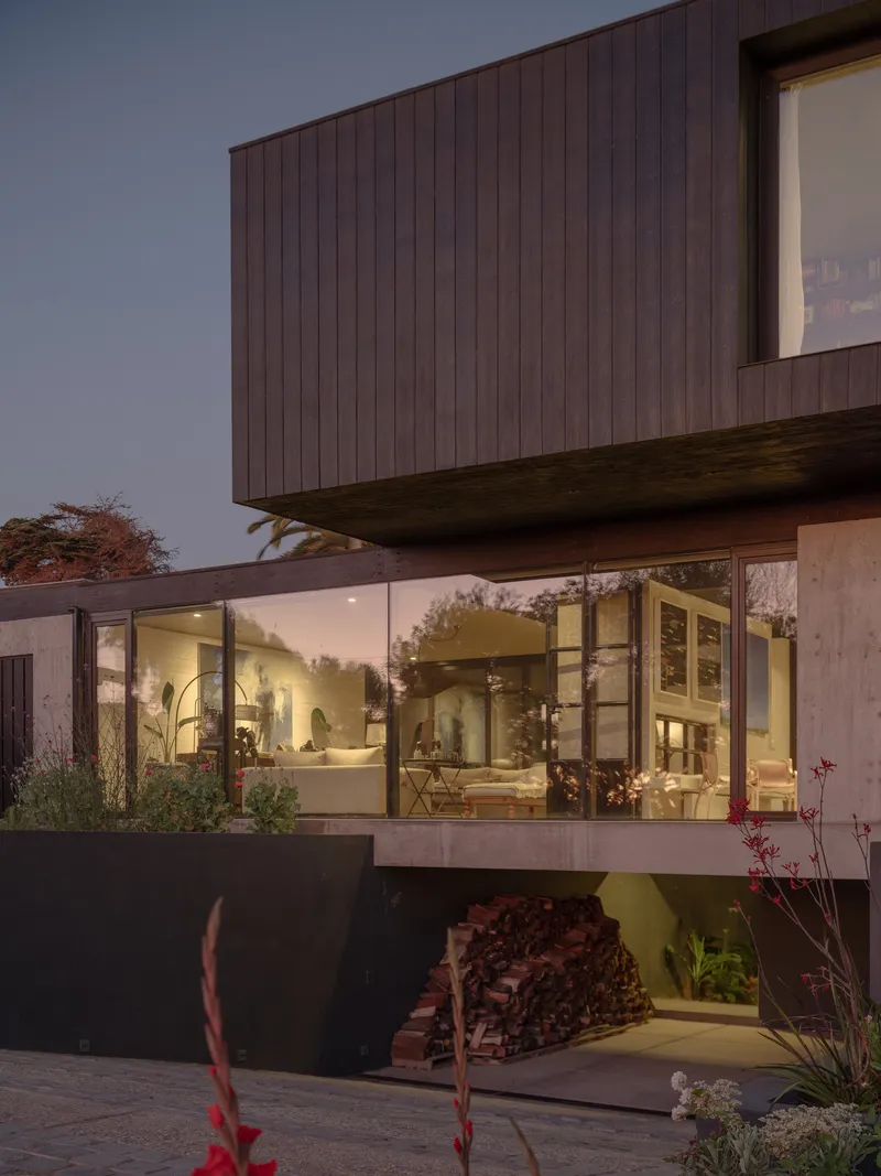 Stacked volumes with timber cladding and glass walls revealing lit interiors at dusk