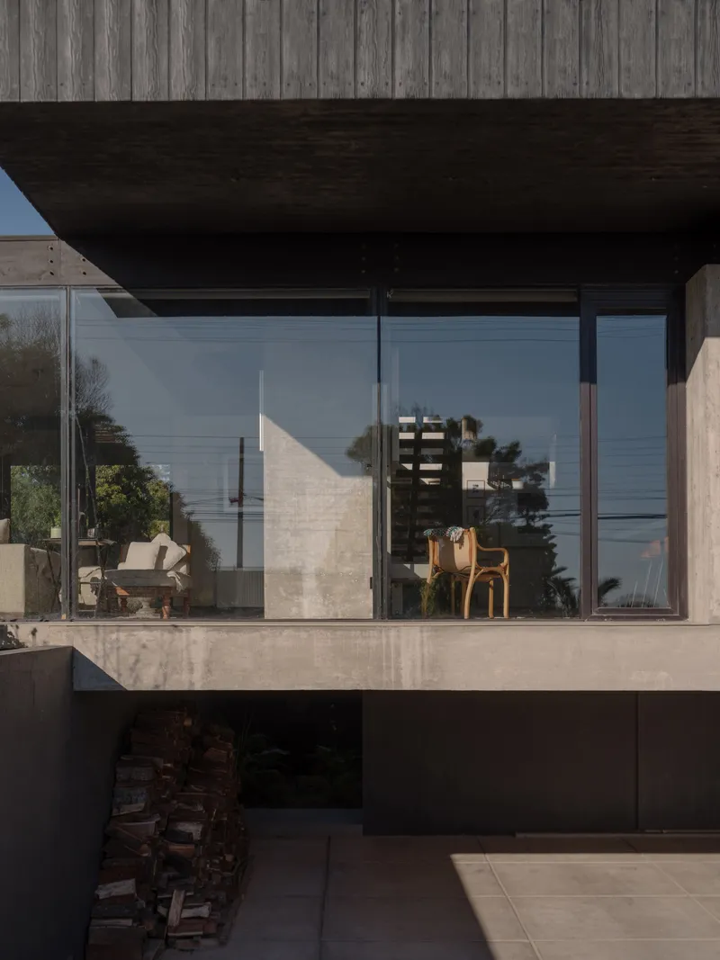 Full-height glazing beneath dark timber soffit reflecting concrete walls and furnishings in afternoon light