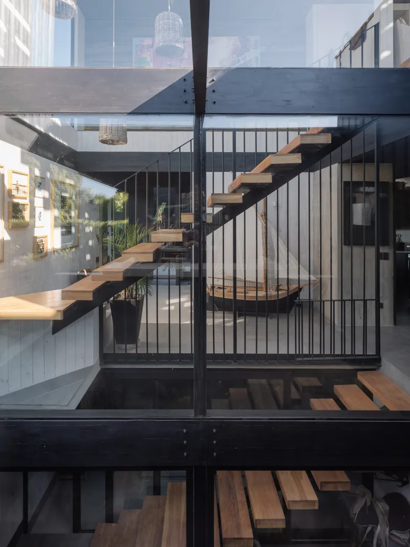 Cantilevered timber treads with black steel structure and vertical rod railings in a daylit interior void