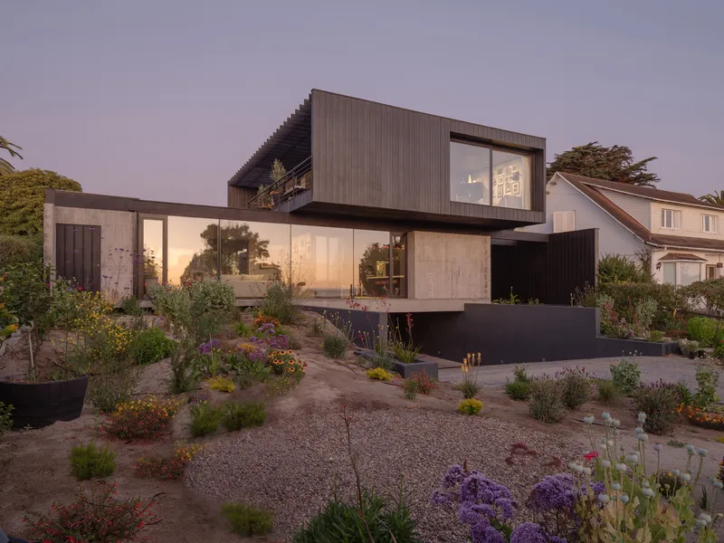 Cantilevered timber-clad volumes above a gravel garden with native plantings at dusk