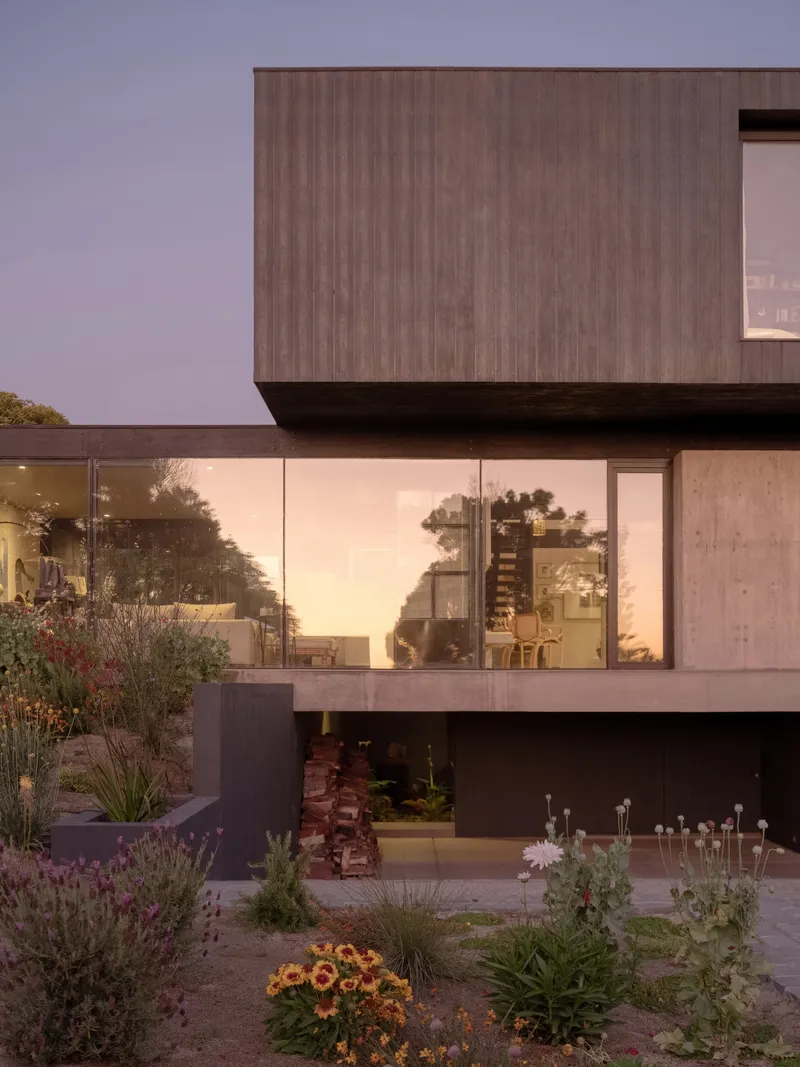 Stacked volumes with timber cladding and floor-to-ceiling glazing overlooking a planted terrace at twilight