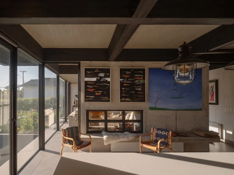Living room with exposed timber beams, concrete fireplace surround, and glazed corner opening to garden