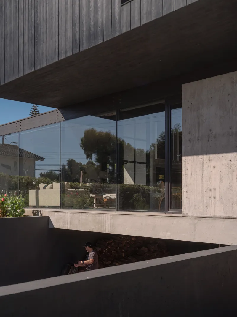 Corner detail of cantilevered concrete plinth with steel-framed glazing and timber soffit above planted bed