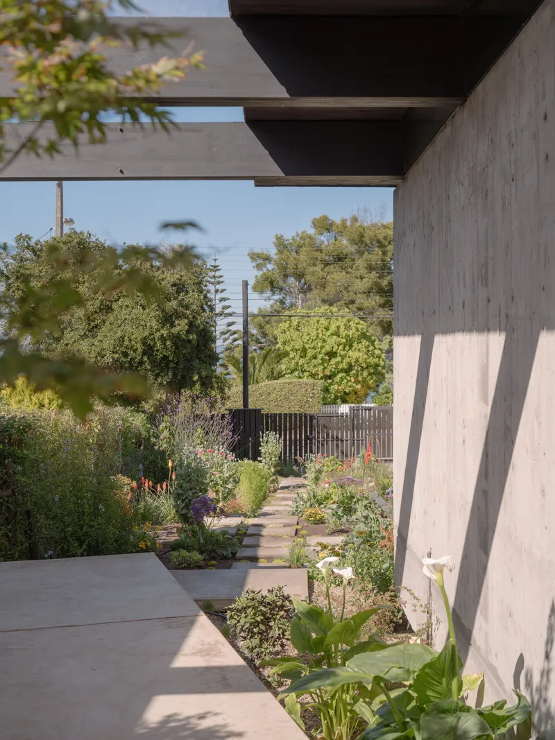 Covered walkway with board-formed concrete columns and beams framing a planted garden path