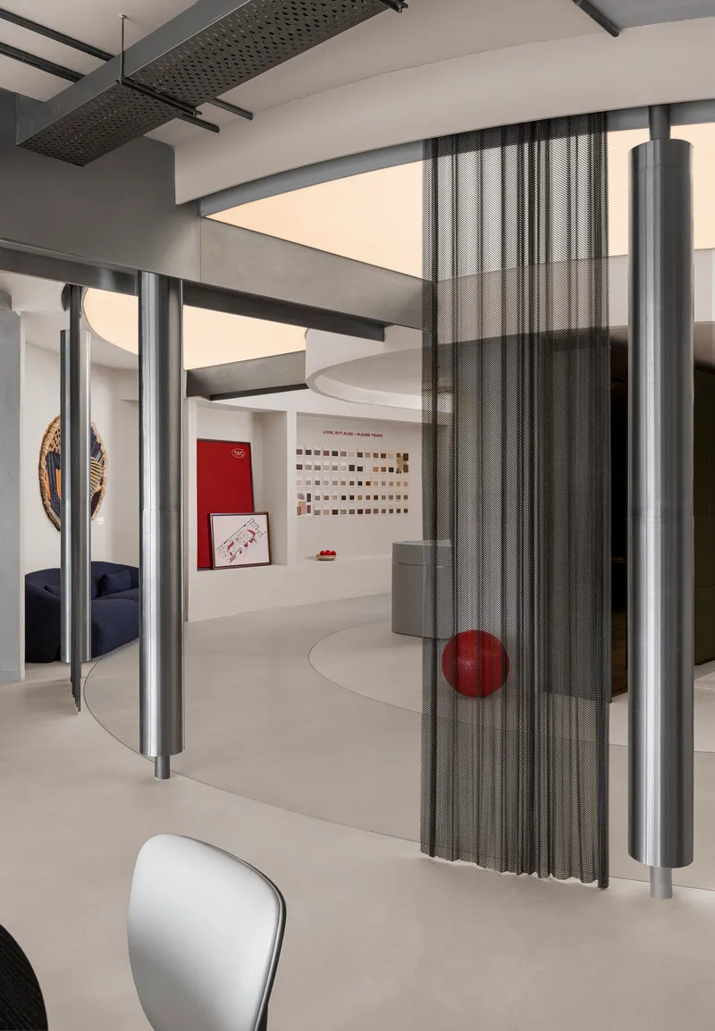 Interior showroom with cylindrical metal screens, curved ceiling soffits and perforated steel beams overhead
