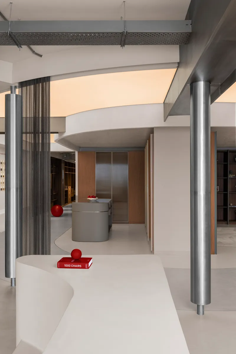 Curving white display counter with metal columns and overhead beams in a retail space