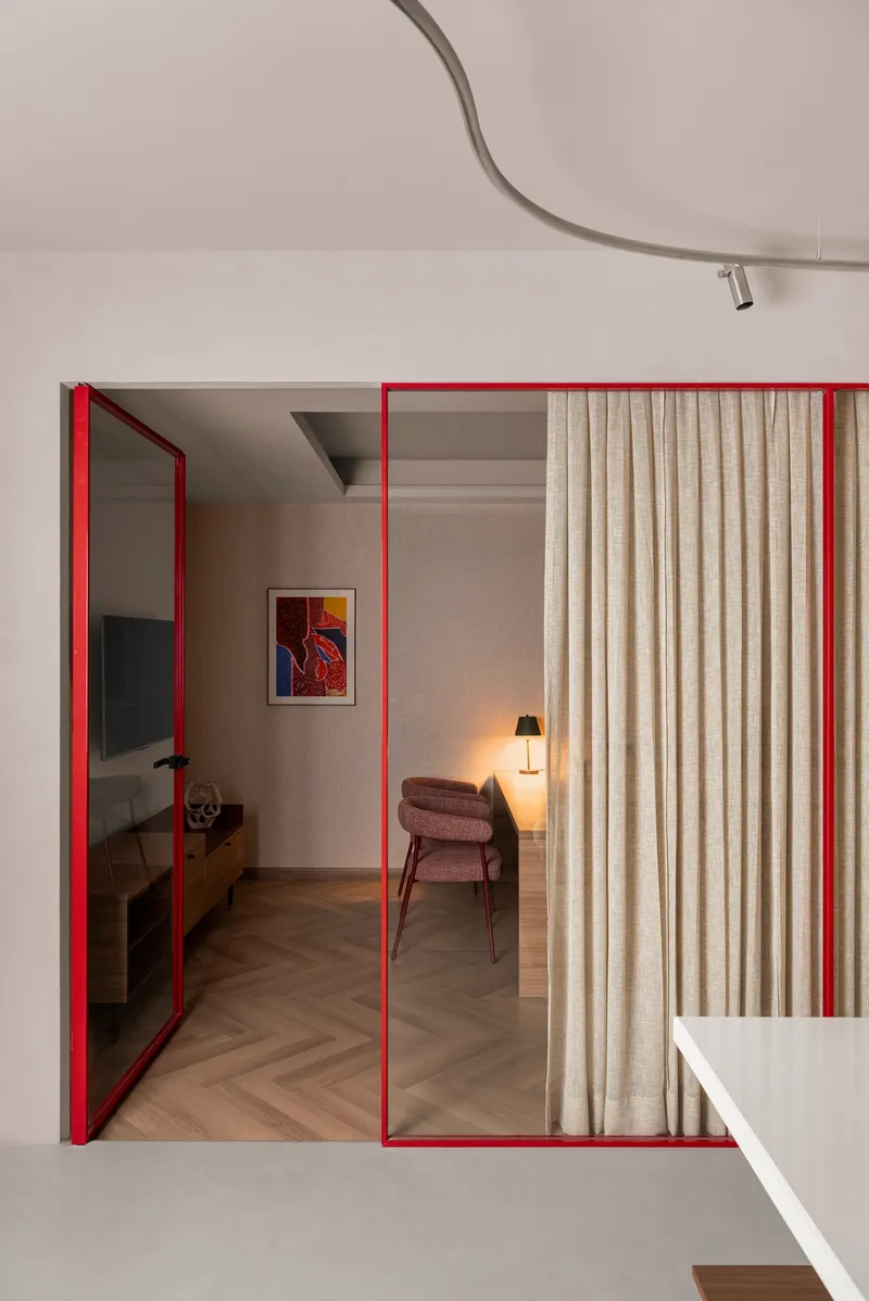 Red steel framed sliding doors with glazing and curtain panels opening to a bedroom beyond