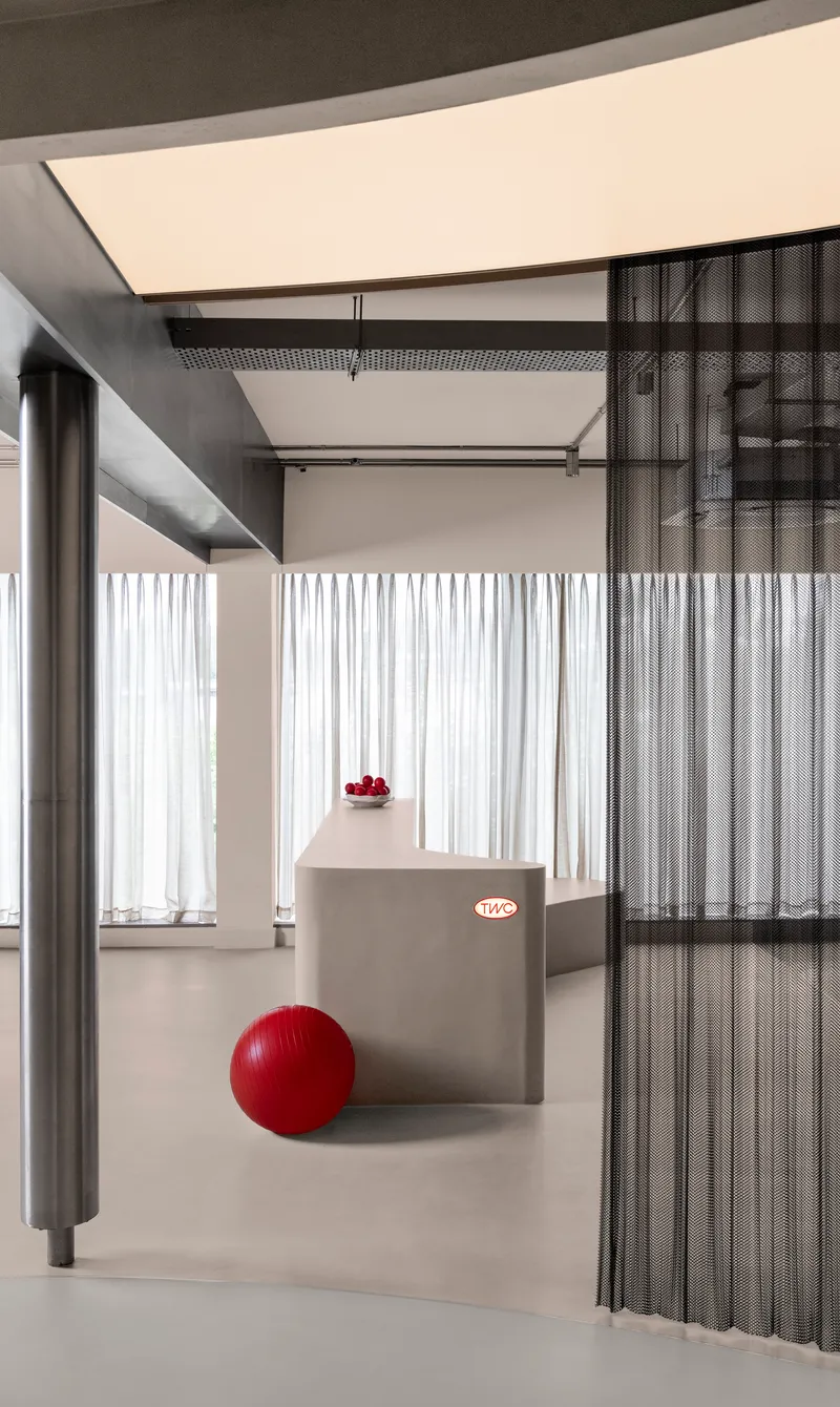 Interior view through metal mesh partition with red exercise ball on the polished floor and sheer curtains beyond