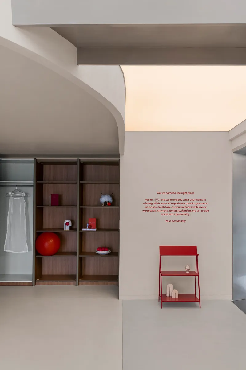 White wall with red text, a curved volume, timber shelving, and a red metal side table