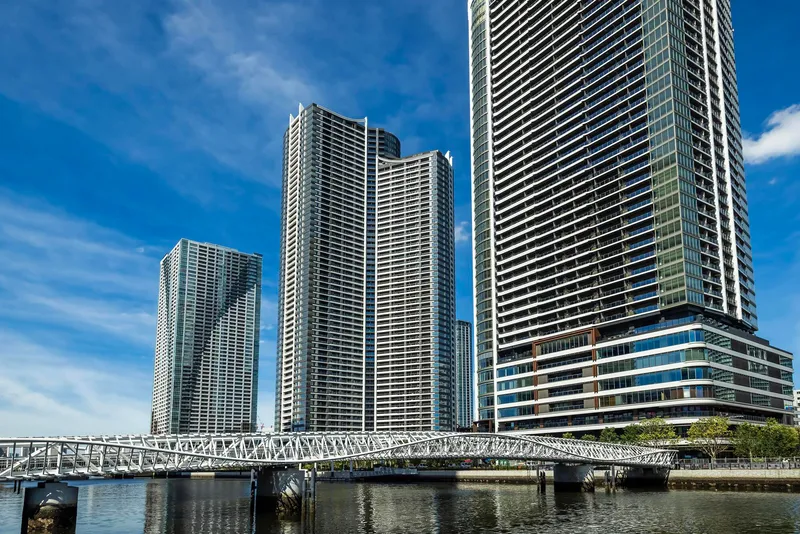 Curved pedestrian bridge with triangulated steel structure crossing waterway beneath residential towers