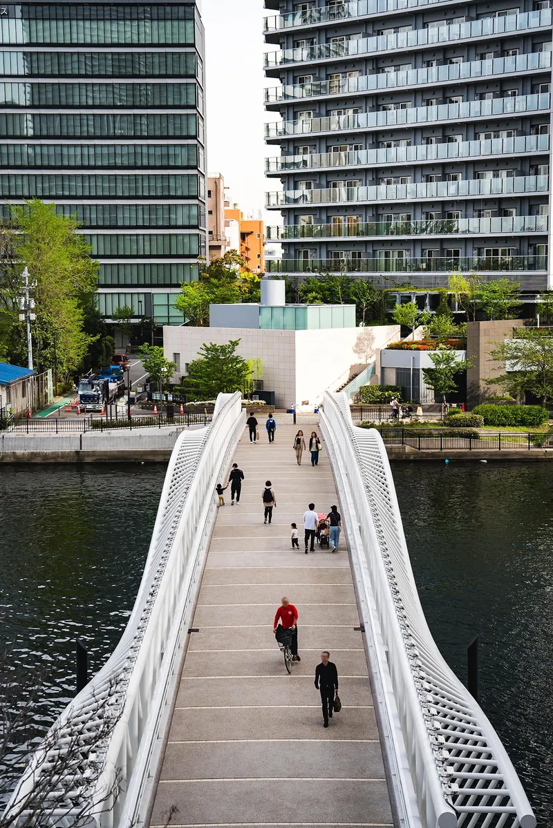 View along the timber deck of the bridge with pedestrians and cyclists moving between glass towers
