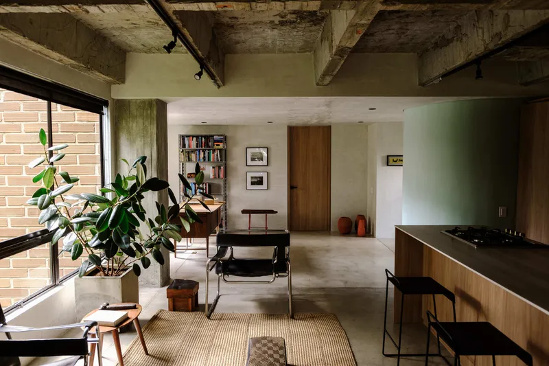 Open living area with exposed concrete ceiling beams and pink brick wall framing a window with potted plants