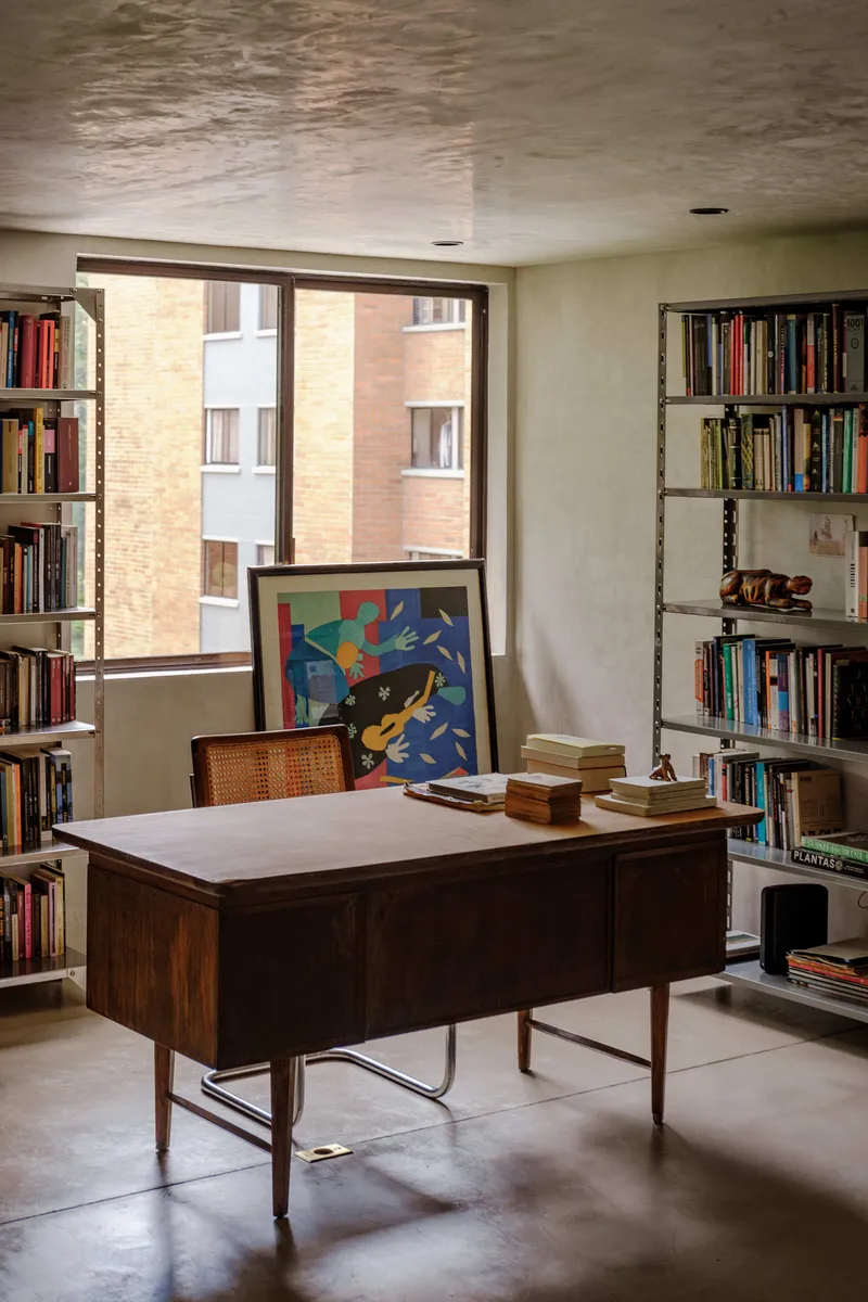 Study corner with wooden desk and flanking bookshelves beneath a window overlooking neighboring brick building