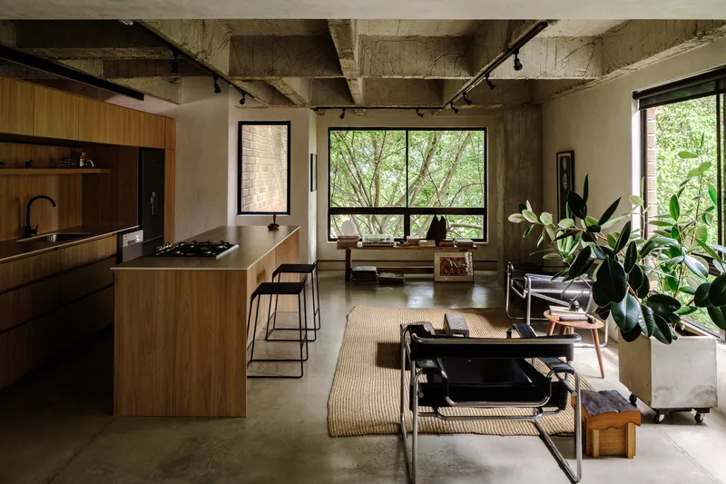 Open kitchen and living space with timber island, concrete floor and large window looking onto trees