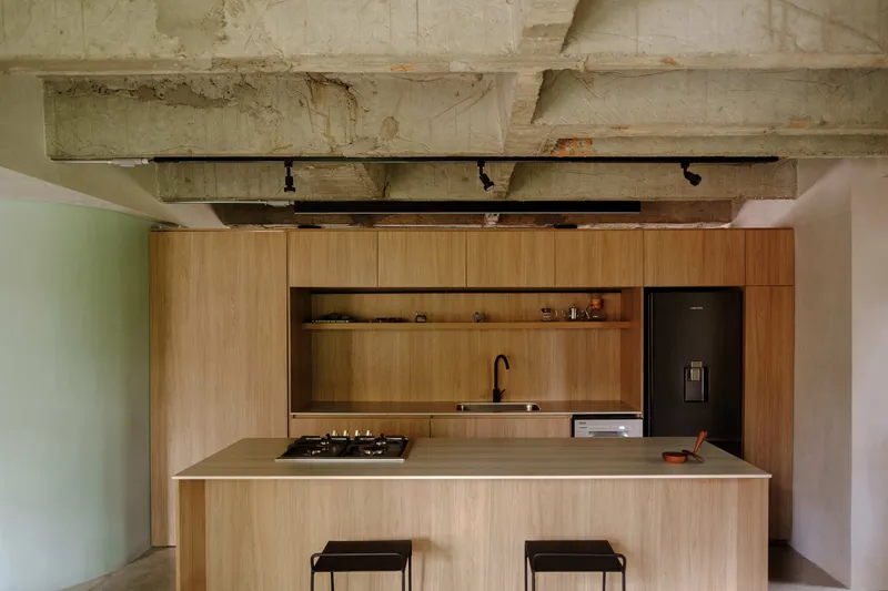 Kitchen island with timber cabinetry and stone countertop below exposed concrete ceiling with black track lighting