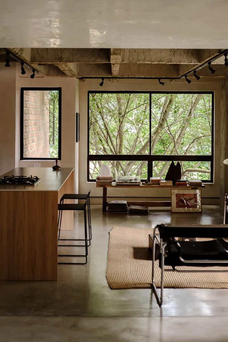 Living area with polished concrete floor looking toward window framed by trees and flanked by kitchen island