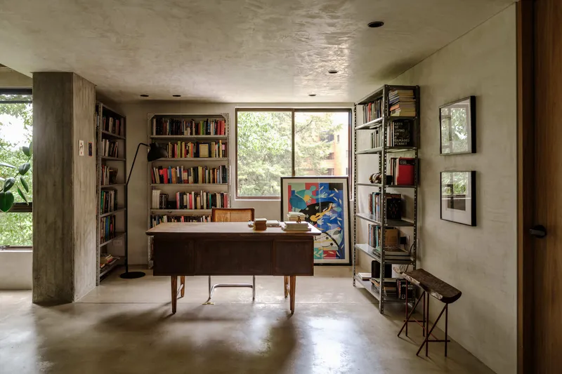 Study space with timber desk, freestanding bookshelves, and concrete columns flanking polished floor
