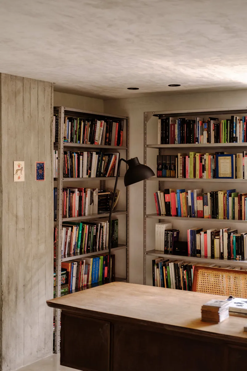 Bookshelf niche between concrete column and plastered wall with task lamp in study corner