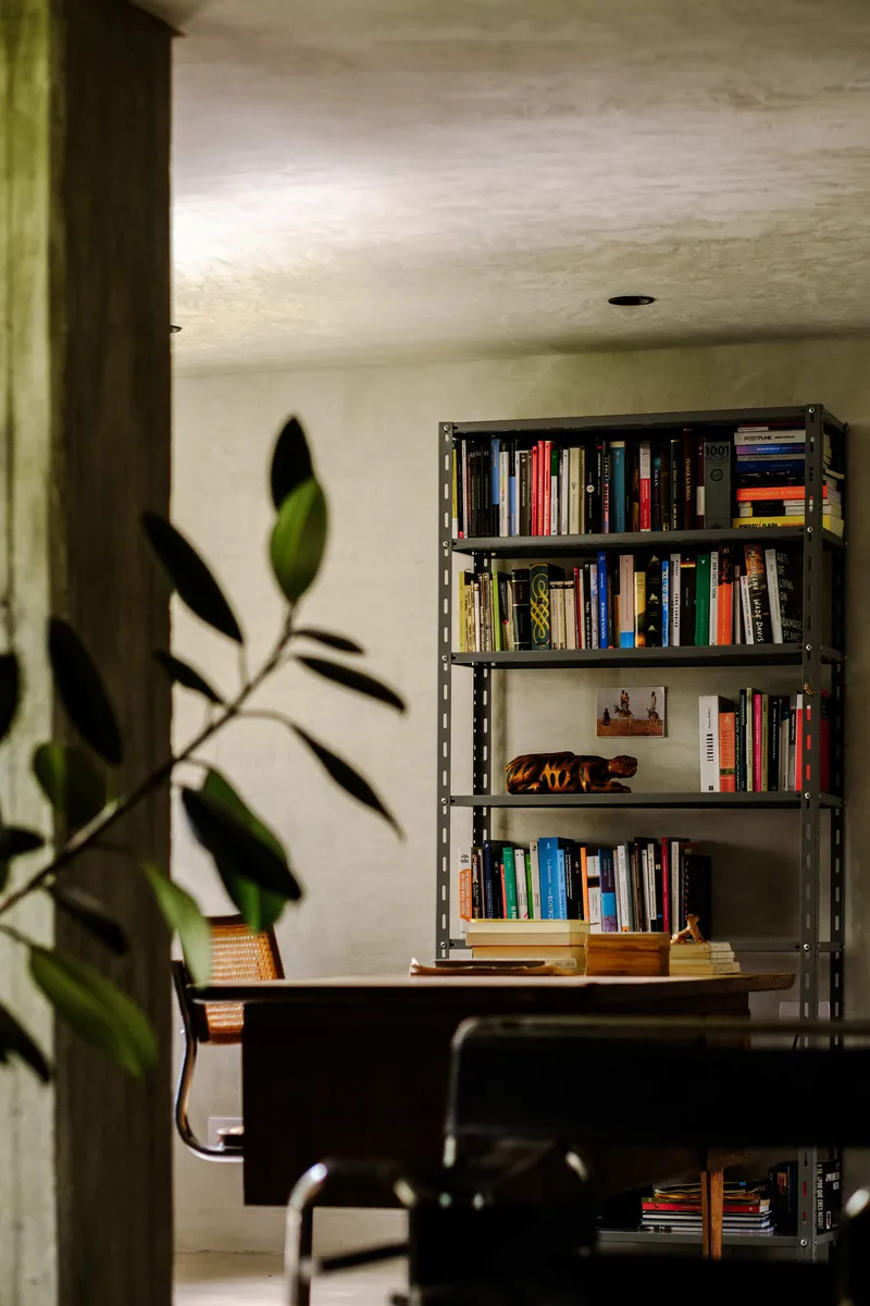 Metal bookshelf unit with desk chair silhouette framed by concrete column and potted plant