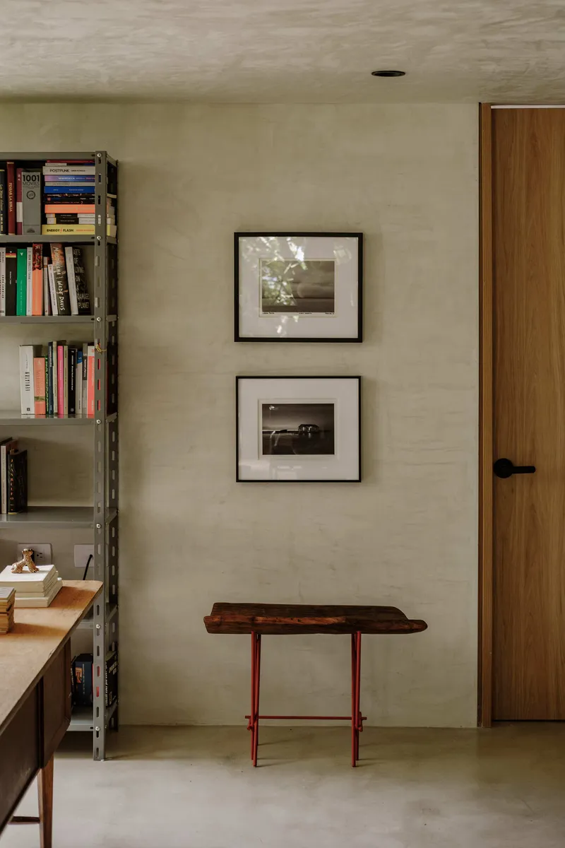 Study nook with industrial shelving, framed photographs on pale plaster walls, and a timber door