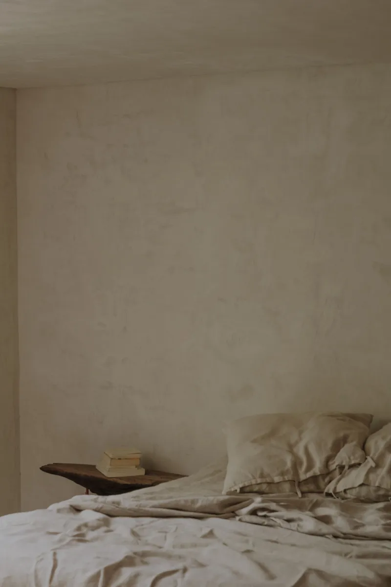 Textured plaster wall meeting the corner above a bed dressed in neutral linen