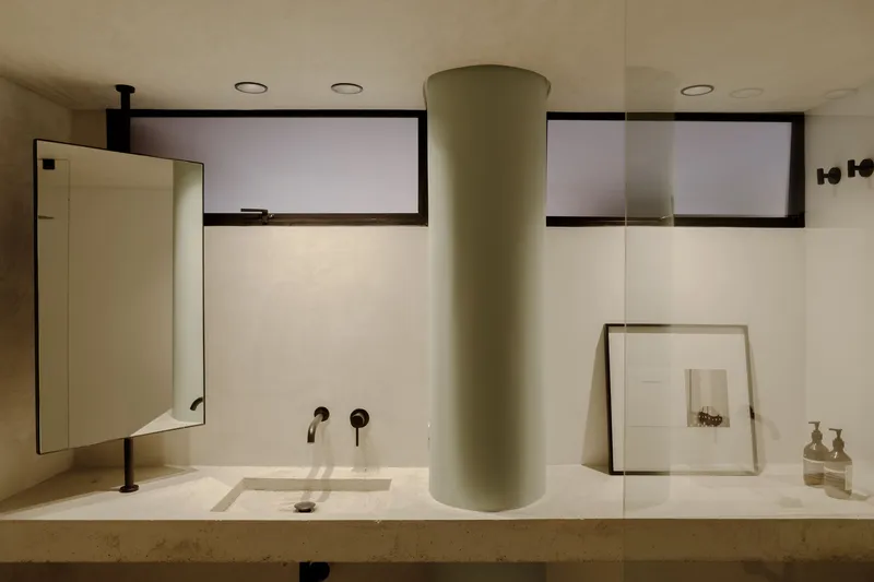 Bathroom vanity with stone countertop, circular column, wall-mounted taps, and horizontal clerestory windows