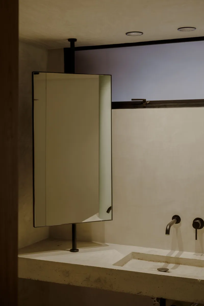 Pivoting mirror cabinet above an integrated sink with matte black fixtures in low evening light
