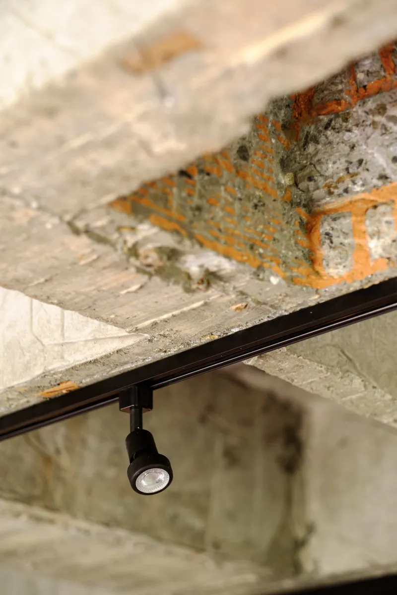 Black track light fixture mounted beneath a distressed concrete ceiling with exposed orange rebar