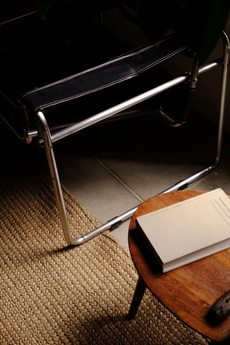 Chrome tubular chair on sisal rug beside a wood side table with an open book