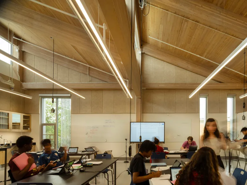 Classroom interior with vaulted timber ceiling, linear pendant lights, and occupants working at tables