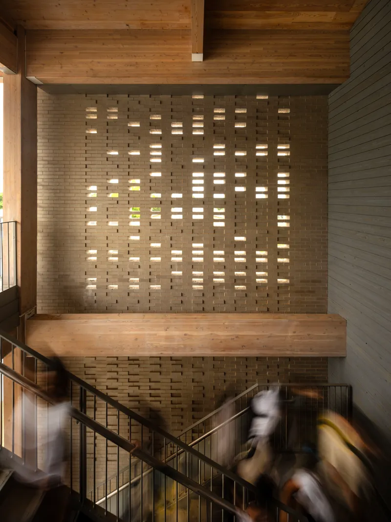 Perforated brick stair wall with light filtering through openings as people descend the steps