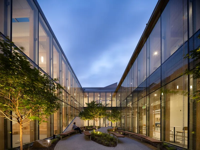 Enclosed courtyard with mesh-clad facades, planted beds, and trees under a twilight sky