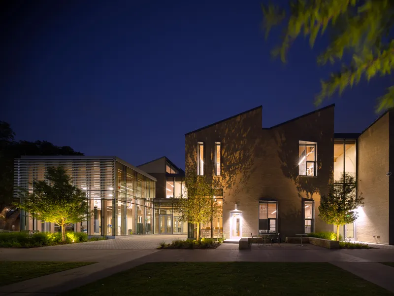 Illuminated complex at night showing the glass-walled wing and angular stone volumes across the plaza