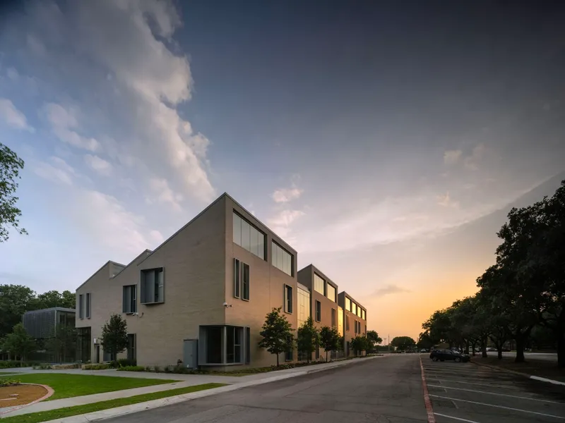 Street view of buff-colored brick facade with sawtooth roofline at dusk