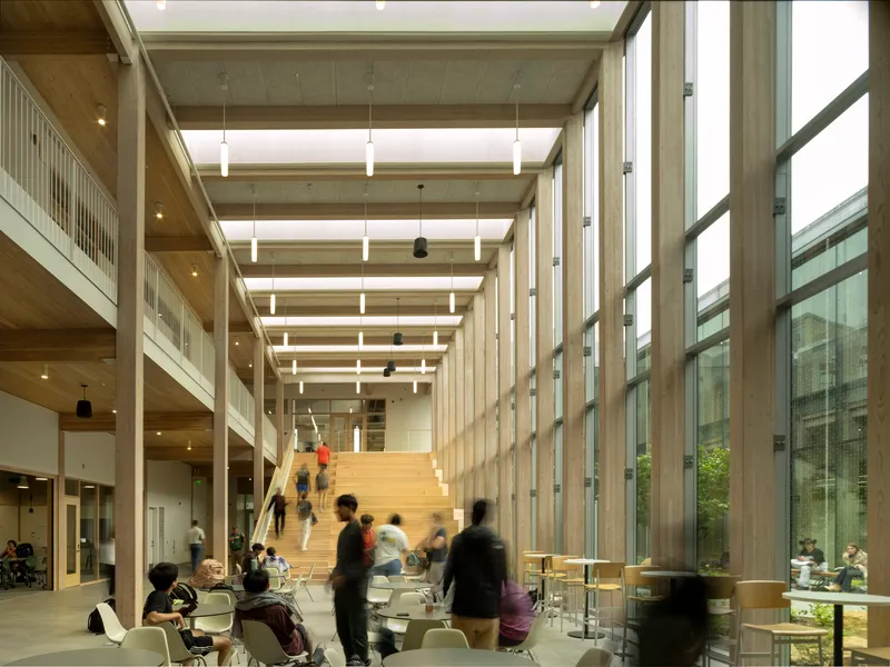 Interior atrium with exposed timber ceiling beams, wide timber staircase and students gathered below