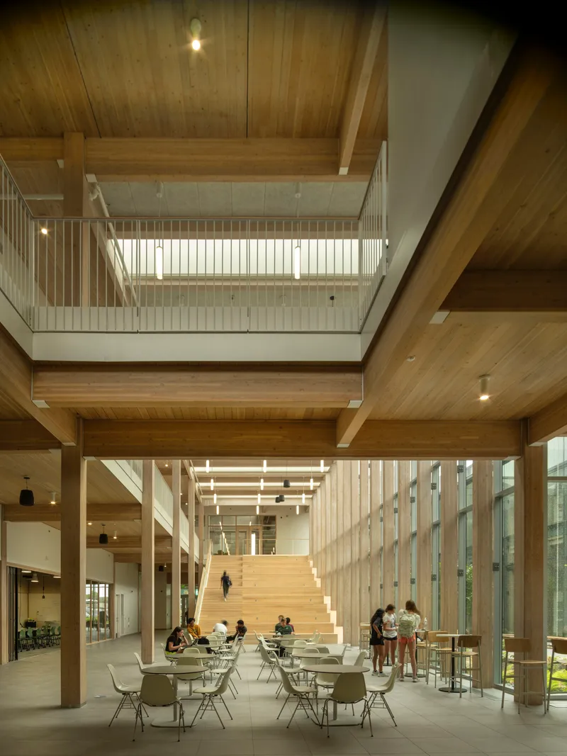 Triple-height atrium with timber beams, clerestory windows and wide staircase with people seated at tables below